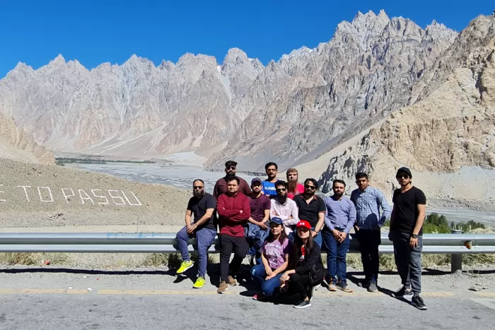 The team at the roadside sign for Passu, with the Cathedral peaks behind them