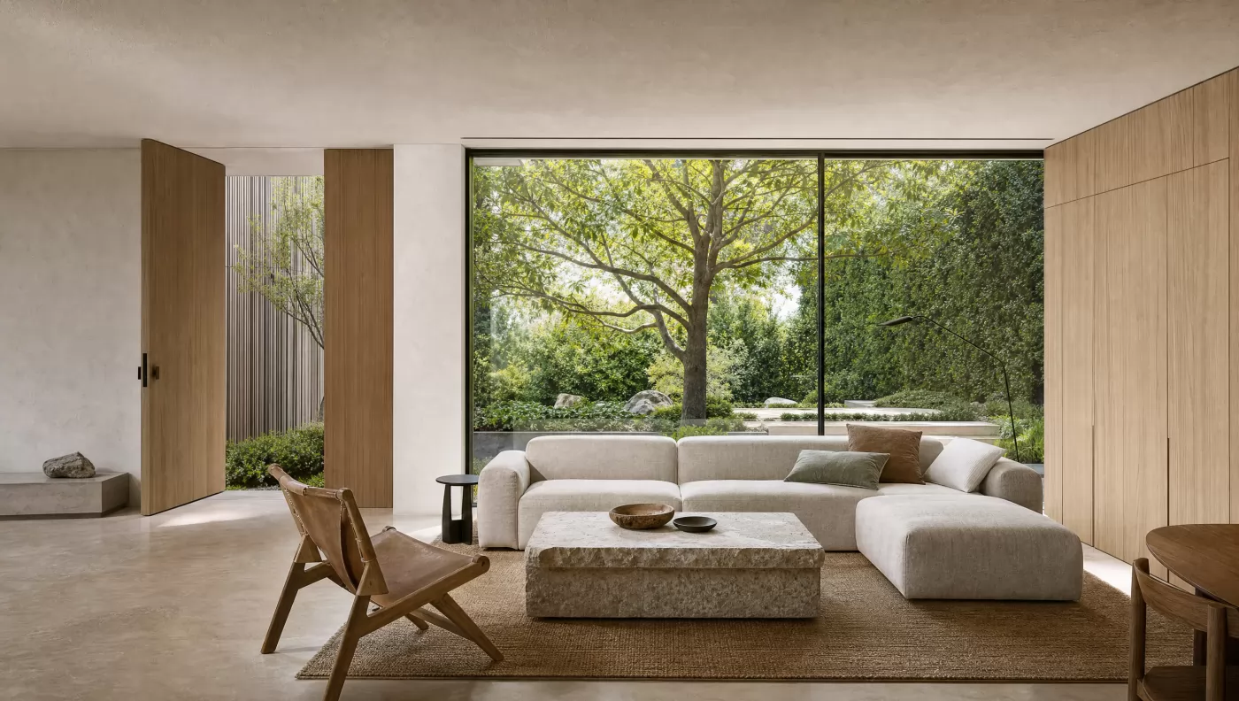 Living room with a low linen sofa and a stone table, facing a full-height window onto a garden